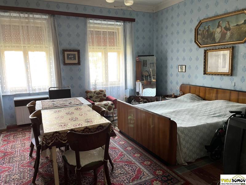 Interior of a family house with a bedroom, table, antique furniture, and decorations on the walls.