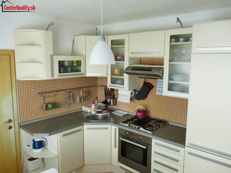 A kitchen in a 3-room apartment with a kitchen unit, appliances, and orange tiles.