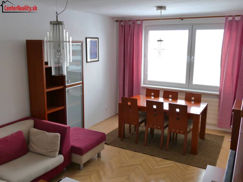 Dining area with a wooden table in a 3-room apartment, complemented by pink curtains and a sofa.