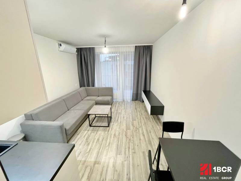 Living room in a studio apartment with a corner sofa and a dining table.