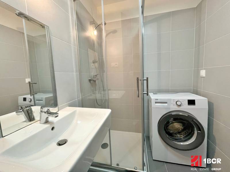 Bathroom with a sink, shower, and washing machine in a studio apartment.