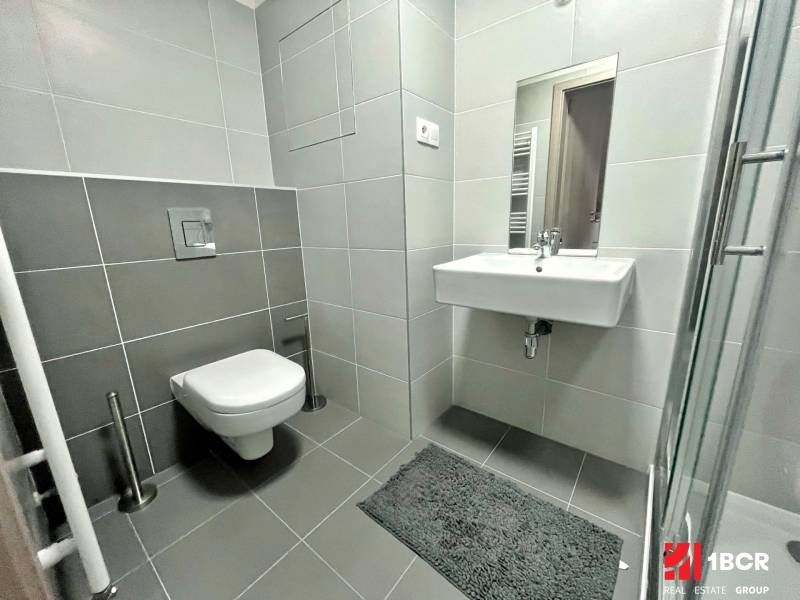 Bathroom in a studio apartment with a shower, sink, and wall-mounted toilet.