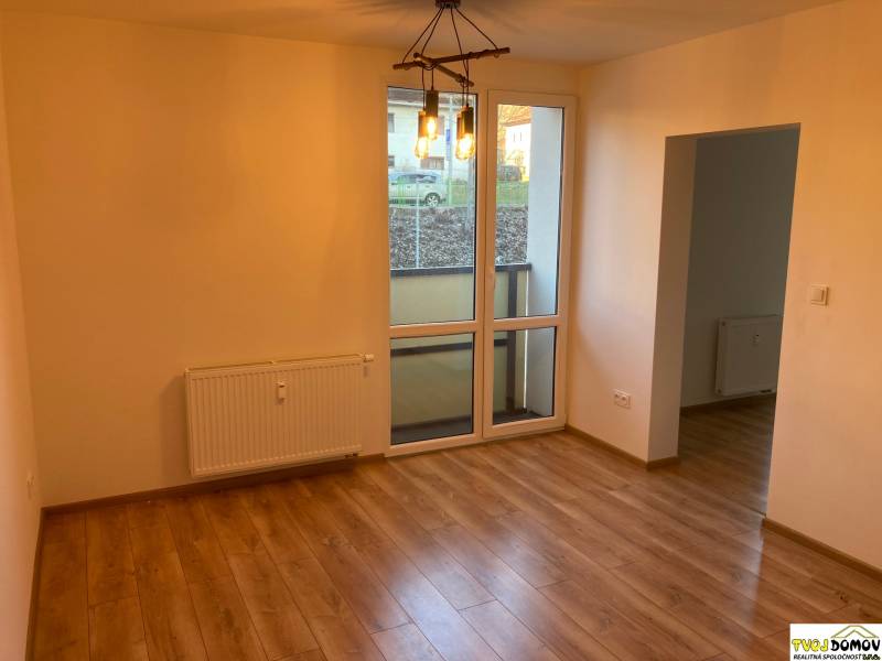 A room with a wooden floor and a large window in a 3-room apartment, simple lighting.
