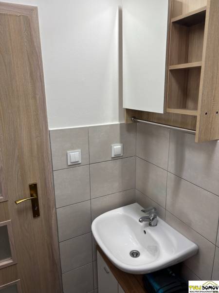 A bathroom in a 3-room apartment with a sink, mirror, and wooden door.