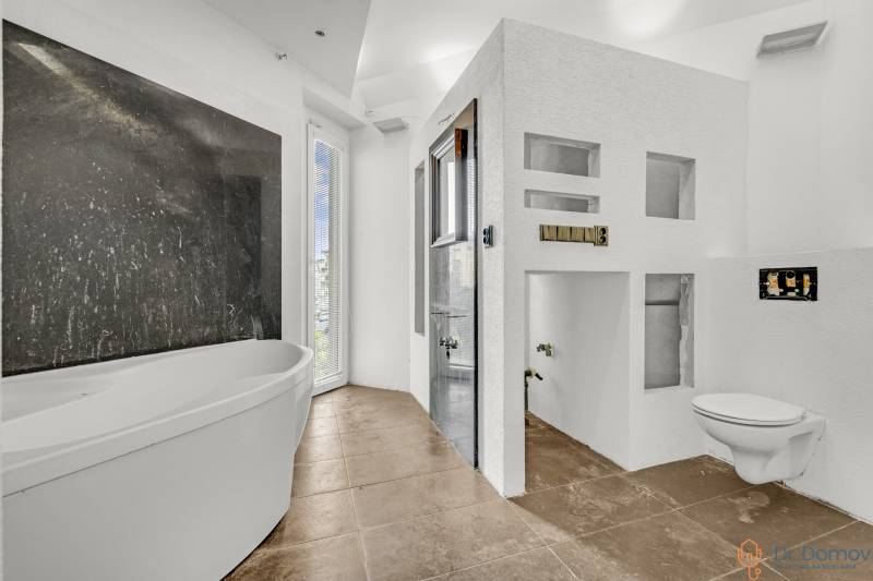 White bathroom with a bathtub, shower, and wall-hung toilet in commercial premises.
