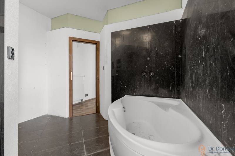 Bathroom with a corner bathtub and black tiles, wooden floor in commercial premises.