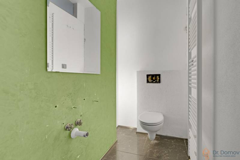Green wall with a connection for a sink, white radiator, and wall-hung toilet in commercial premises.