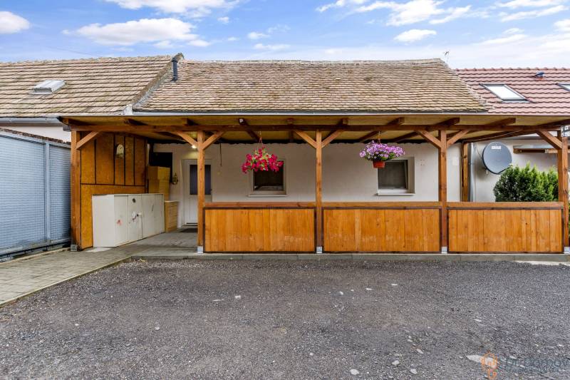 The exterior of a wooden shelter in Malé Leváre in front of a 2-room apartment with flower pots.