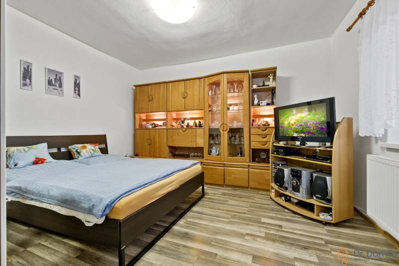 Bedroom with a double bed, wooden living room wall unit, and television in a two-room apartment.