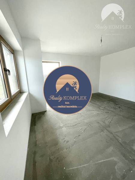 An unfurnished room in a family house with a concrete floor and windows.