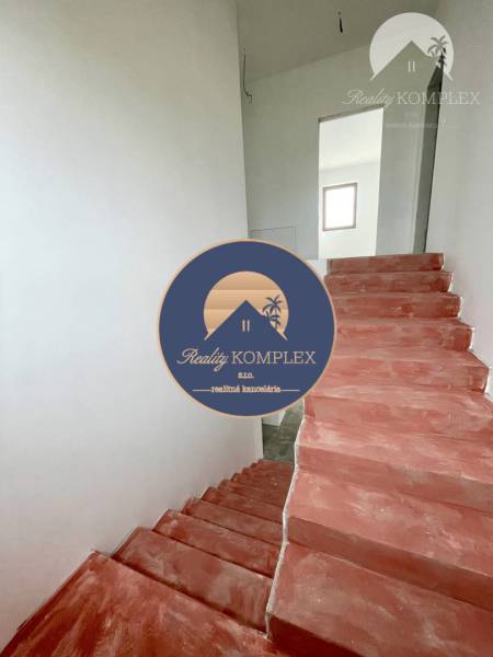 In the family house, there are concrete stairs and white walls leading to the upper floor.
