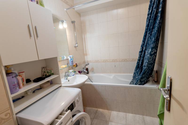 A bathroom in a 4-room apartment with a bathtub, washing machine, and open cabinet.