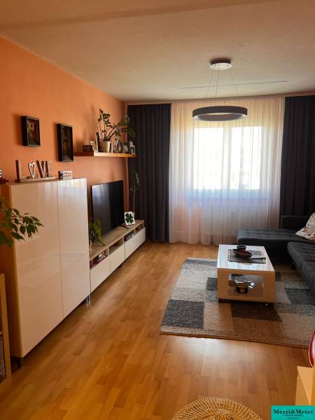 Living room with an orange wall, dark curtains, a large window, and furniture in a three-room apartment.