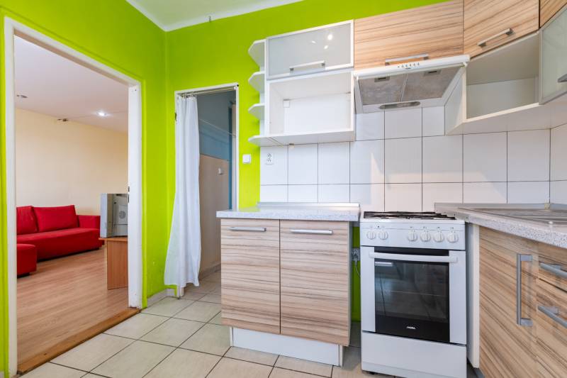 A bright kitchen in a one-room apartment with green walls and wooden cabinets.