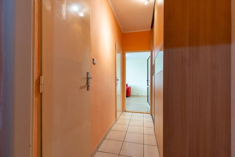 A hallway with orange walls, tiles, and a door to a room in a one-bedroom apartment.