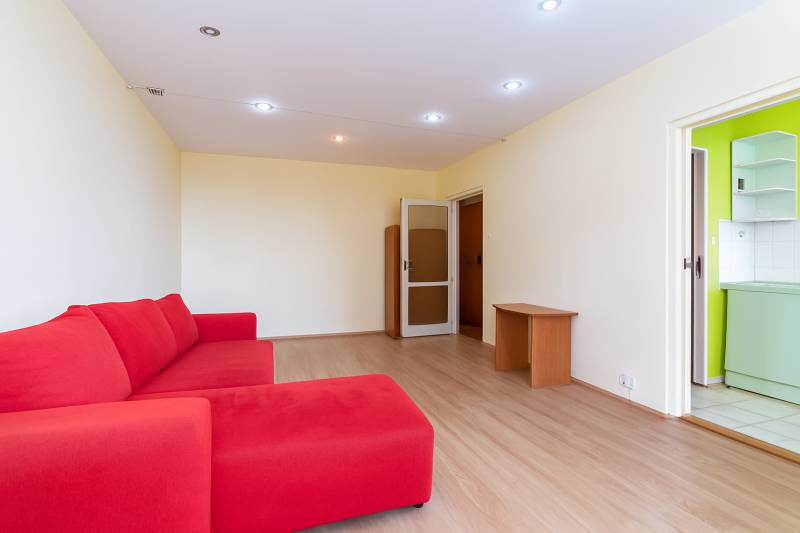Living room with a red sofa, wooden floors, and doors to the kitchen.