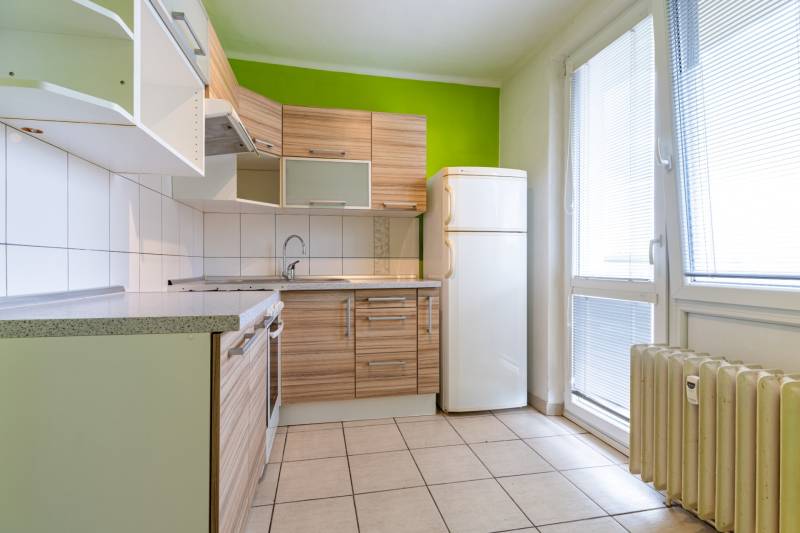 A kitchen in a studio apartment with wooden cabinets, a green wall, and a spacious area.