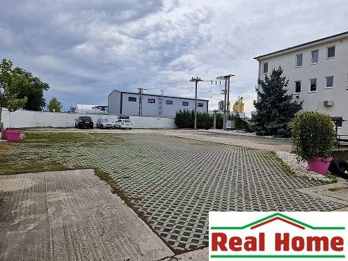 Parking lot on Šamorínska Street near warehouses and halls, marked with a real estate agency sign.