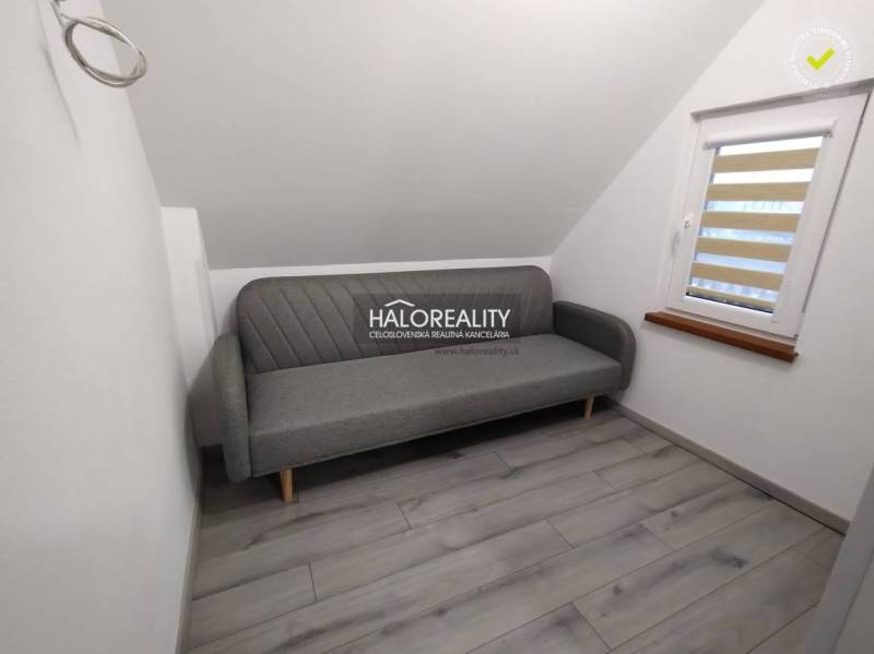 Studio apartment with a gray sofa, white walls, and a window with blinds.