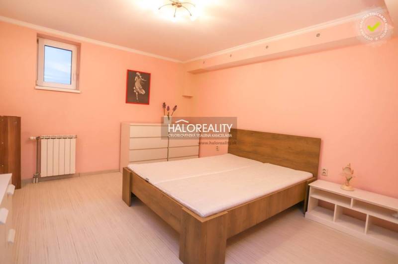 A bedroom with a bed in a 2-room apartment with a spacious dresser and a pastel pink wall.