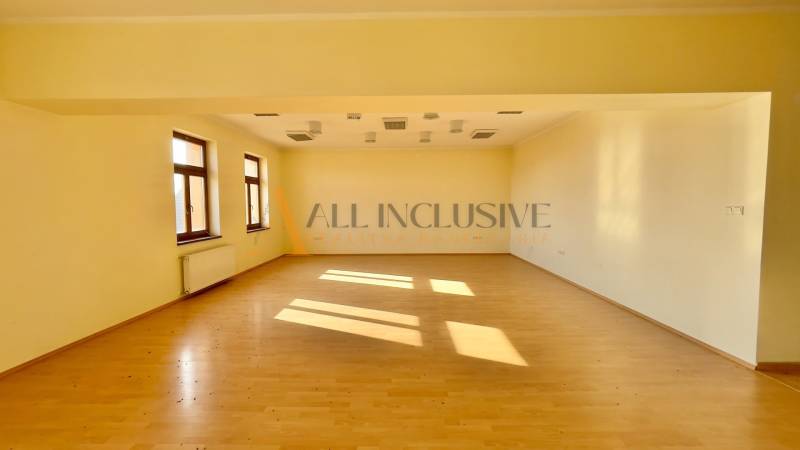 Interior of a building with light walls, wooden floor, and large windows.