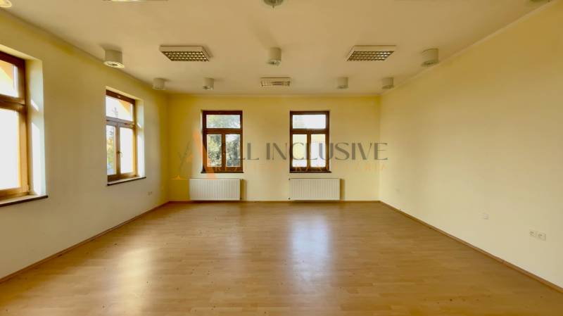A spacious room with wooden flooring, white walls, and multiple windows in a building.