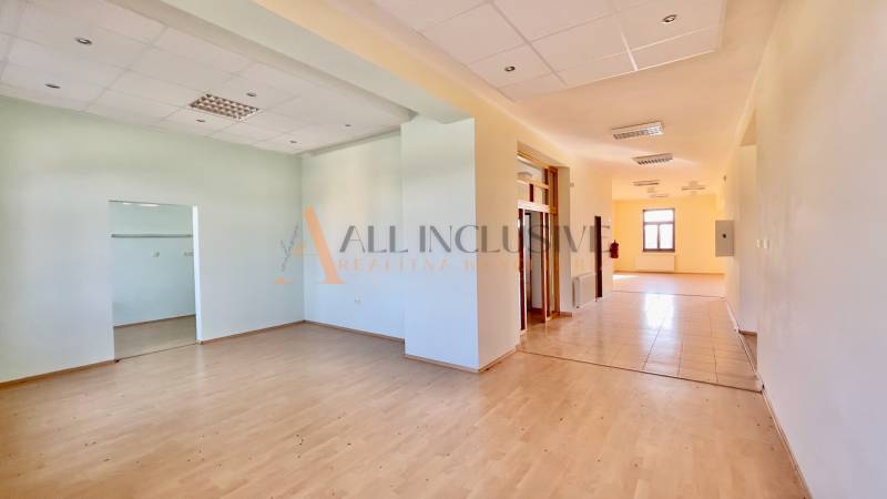 A spacious interior of a building with laminate and tile flooring, separate rooms, and a backlit ceiling.