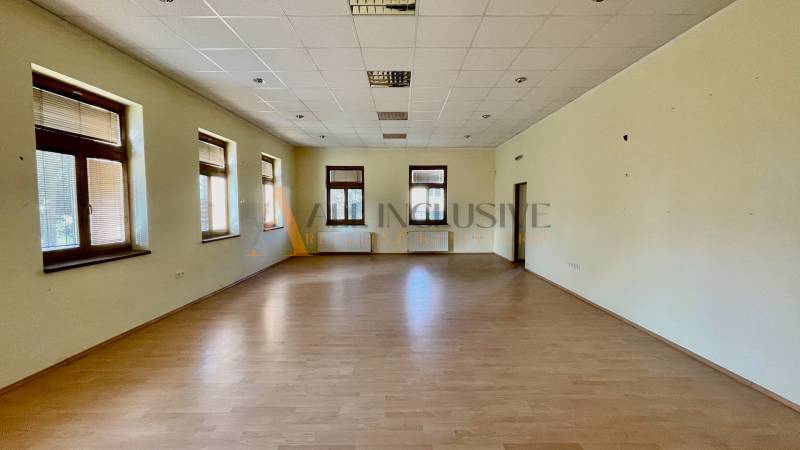 Spacious room in a building with wooden flooring and multiple windows.
