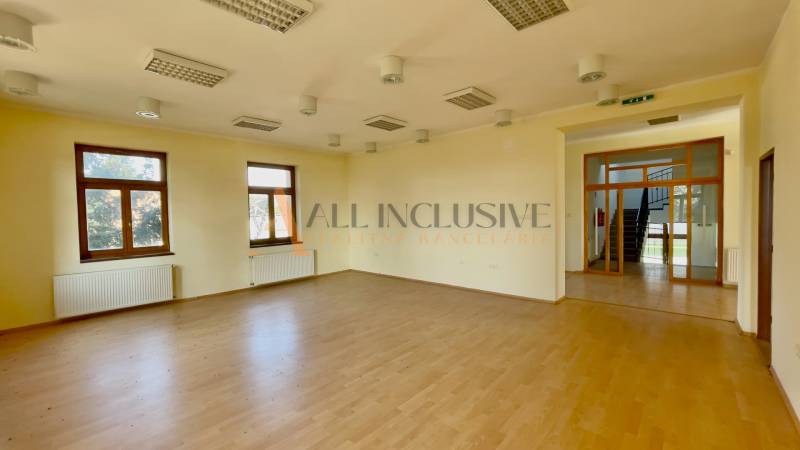 A spacious room with wooden flooring and multiple windows.