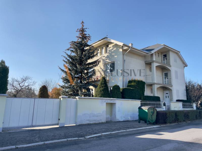 A villa on Športovcov Street in Topoľčany with trees and a garbage container.