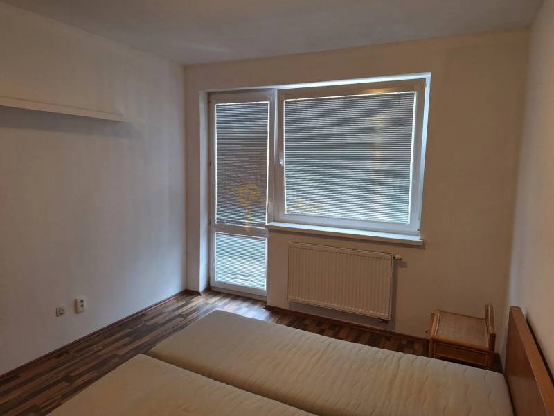 Bedroom in a two-room apartment with a bed and a window with blinds.