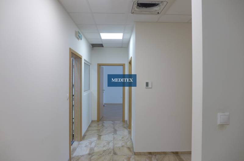 A white corridor with tiles, wooden doors, and lighting in the area of warehouses and halls.