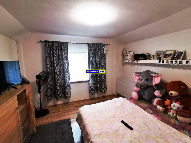 Children's room in a family house with curtains, a bed, a shelf, and stuffed toys.