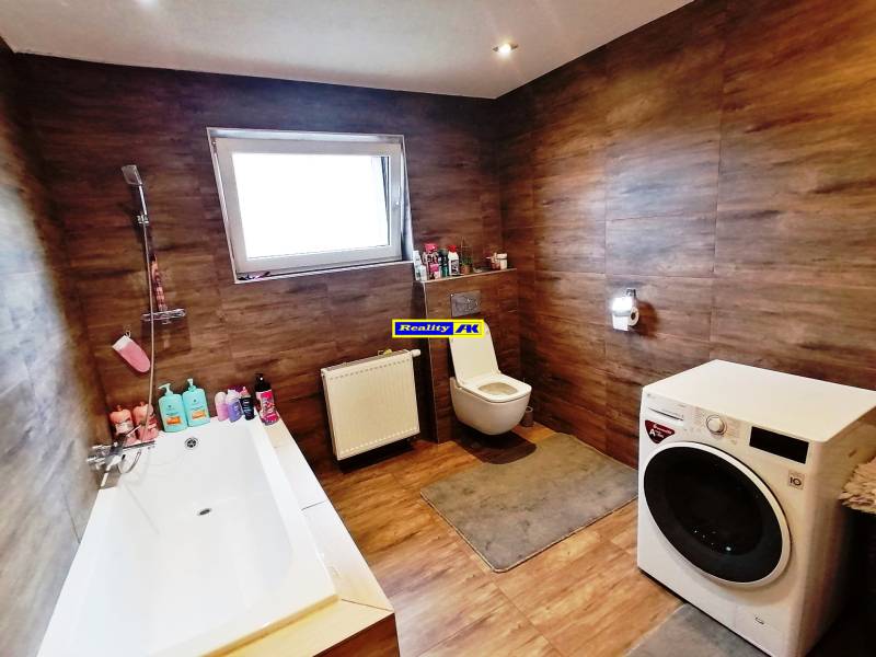 A bathroom in a family house with a bathtub, washing machine, and wooden paneling.