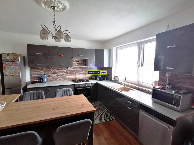 A kitchen in a family house with dark furniture, spacious windows, and a wooden table.