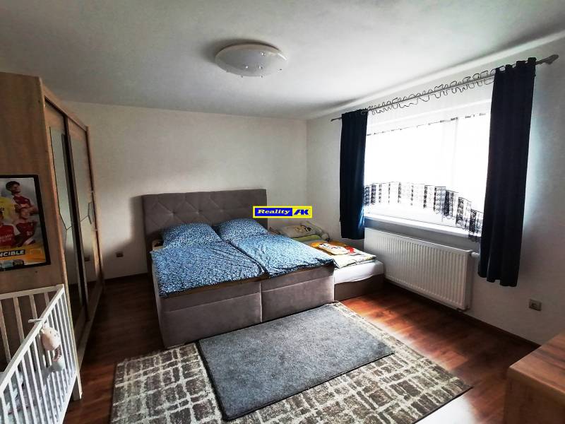 Bedroom in a family house with a bed, cabinet, carpets, and a window with a dark curtain.