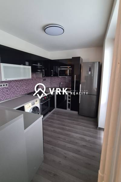 A kitchen in a 2-room apartment with appliances, dark furniture, and purple tiles.