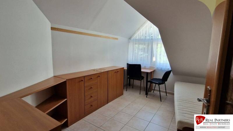 A room in a family house with storage space, two chairs, and a window with curtains.