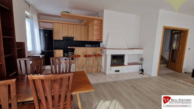 Living room in a family house with a fireplace, kitchen, and wooden furniture.