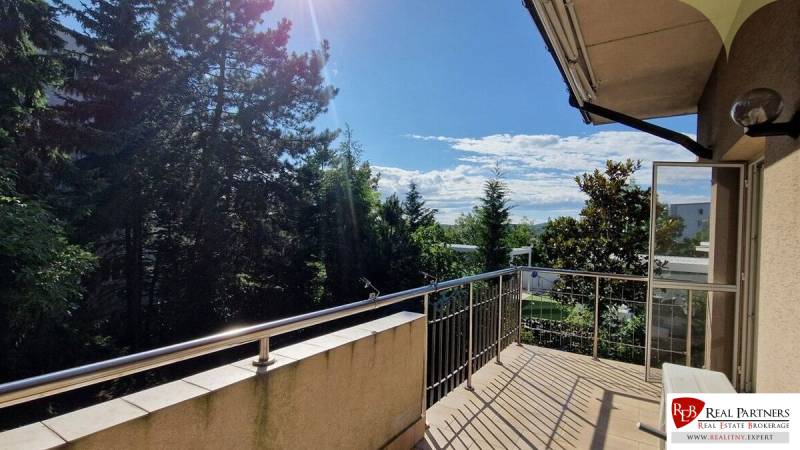 A balcony of a family house with a view of trees, sunny day, open doors.