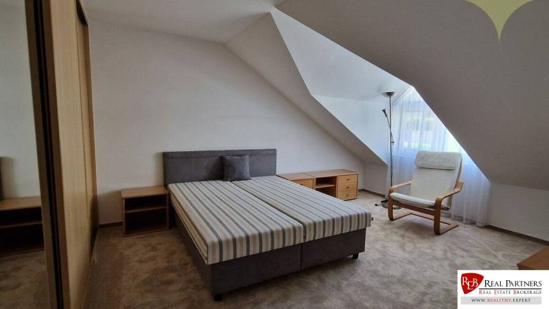 A bedroom with a bed and an armchair in a family house, light walls, sloped roof.