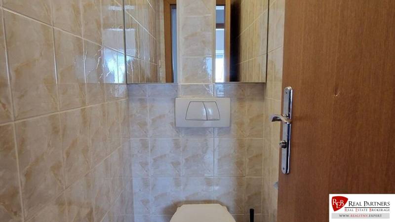 Toilet in a family house with wall tiles and a wall-mounted flush.