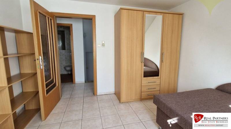 A room in a family house with a bed, wardrobe, shelves, and a bathroom.