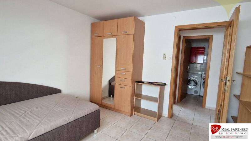 A room in a family house with a bed, a wardrobe, and a view into the bathroom with a washing machine.