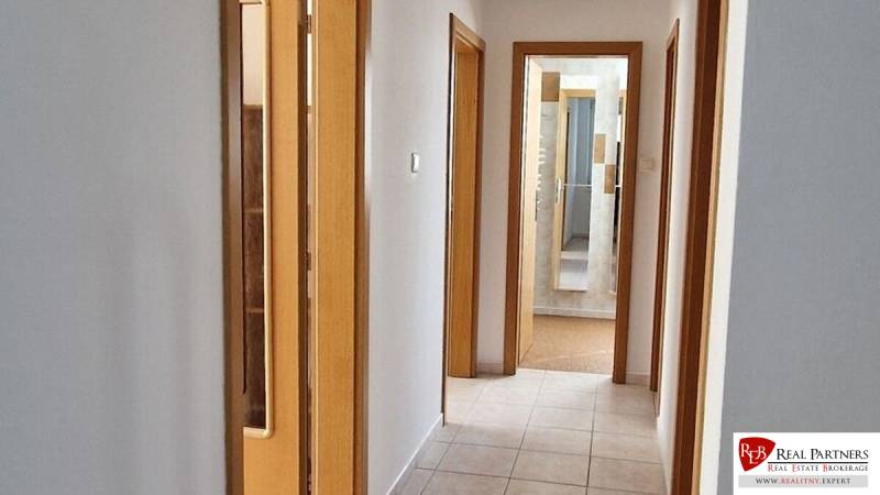 A hallway in a family house with doors, tiles, and a view into the bathroom.