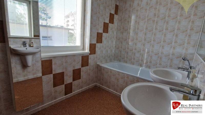A bathroom with a bathtub and sinks in a family house, with tiles and a window.