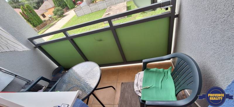 A balcony of a 3-room apartment with a plastic chair and a small glass table.