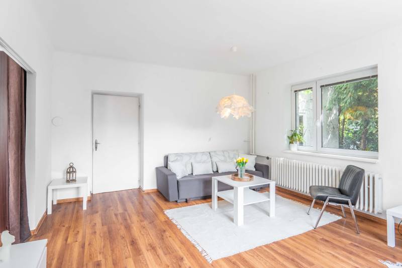 Living room in a two-room apartment with wooden flooring, a sofa, and stylish lighting.