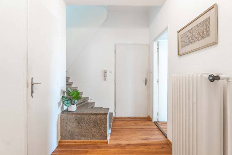 A hallway with a wooden floor, staircase, picture, and radiator in a 2-room apartment.