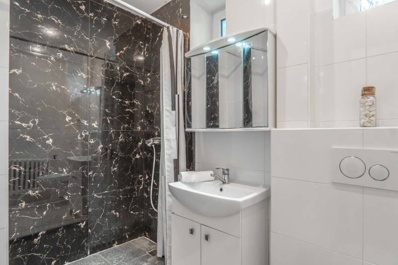 A bathroom in a 2-room apartment with dark marble tiles and a shower corner.